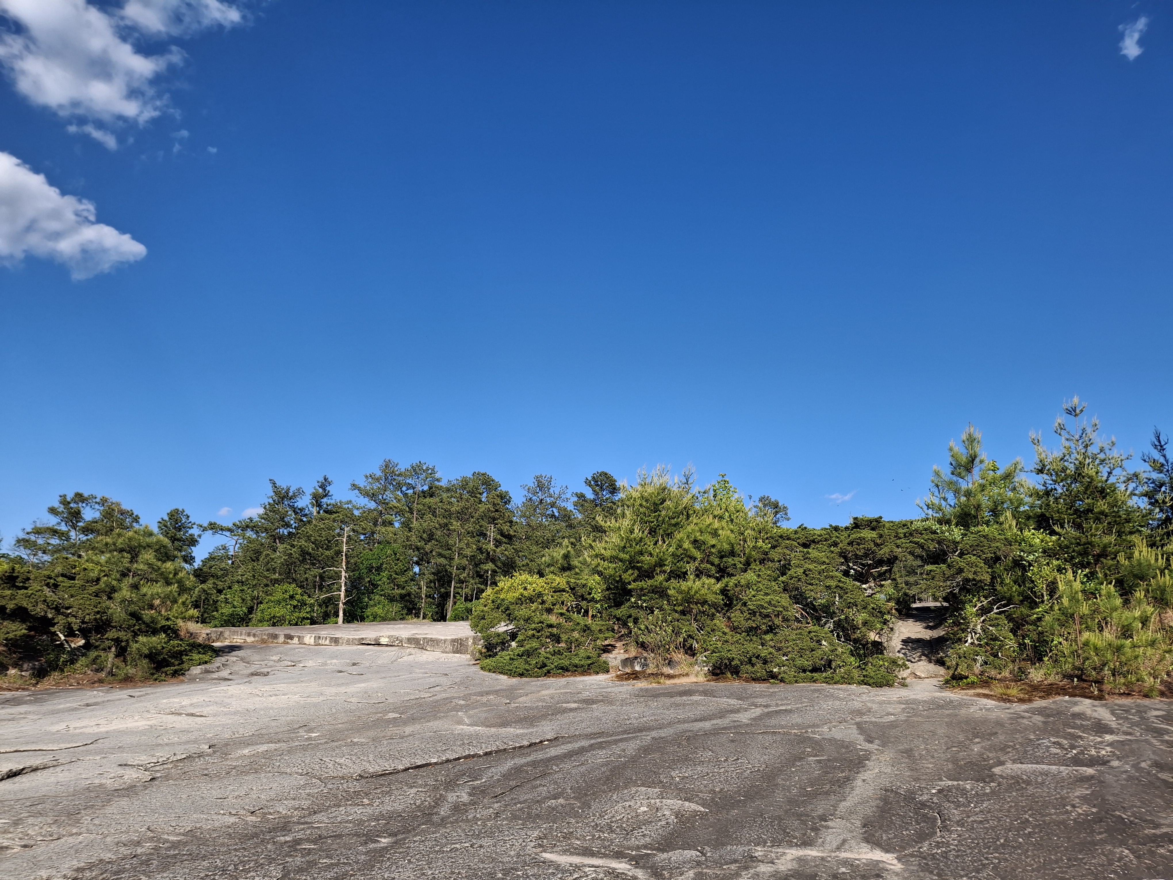 Granite slab foreground, pine horizon, wide blue sky with scattered clouds.