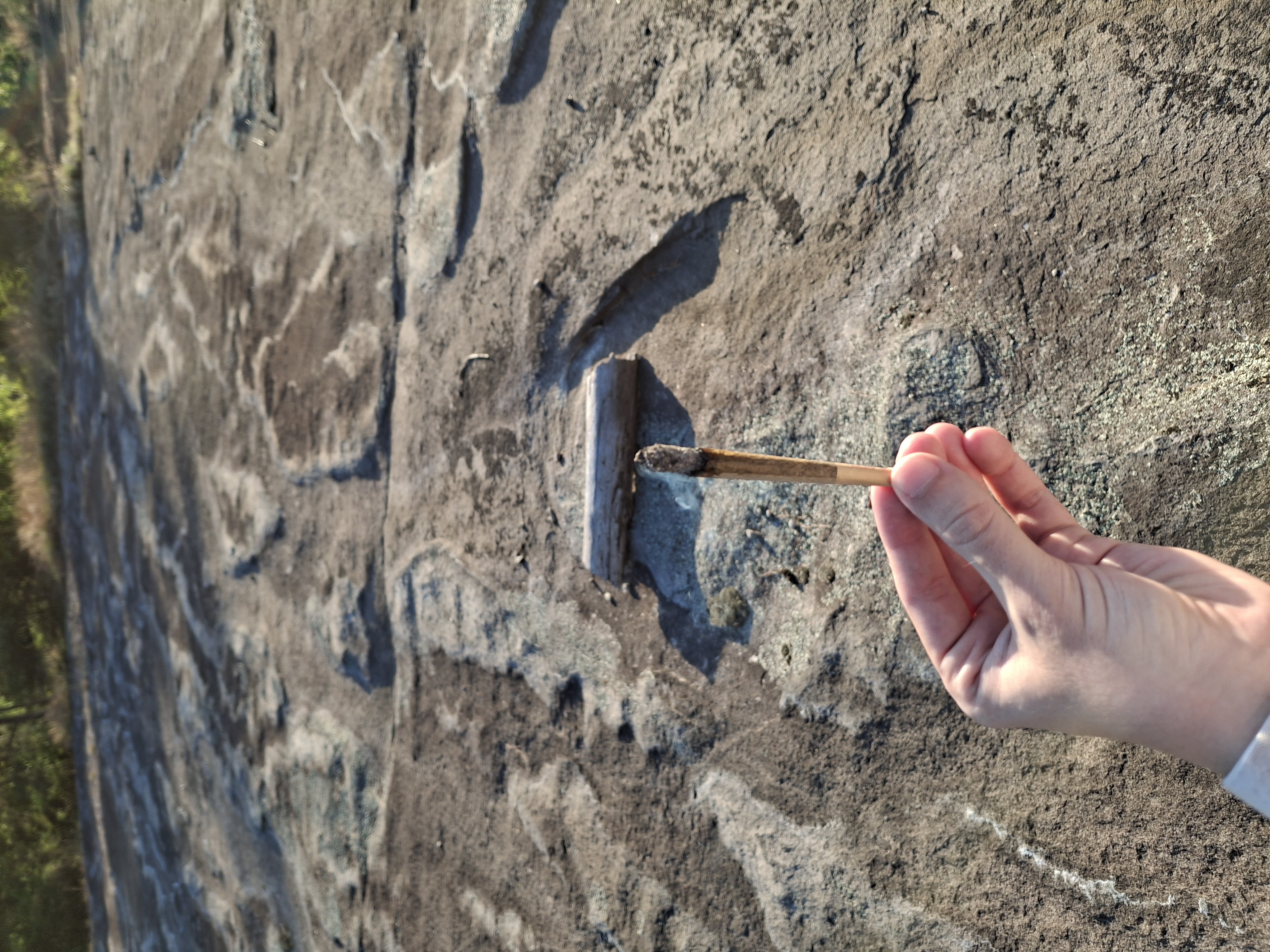 A hand steadies a joint balanced on a small wooden stand set into the granite.