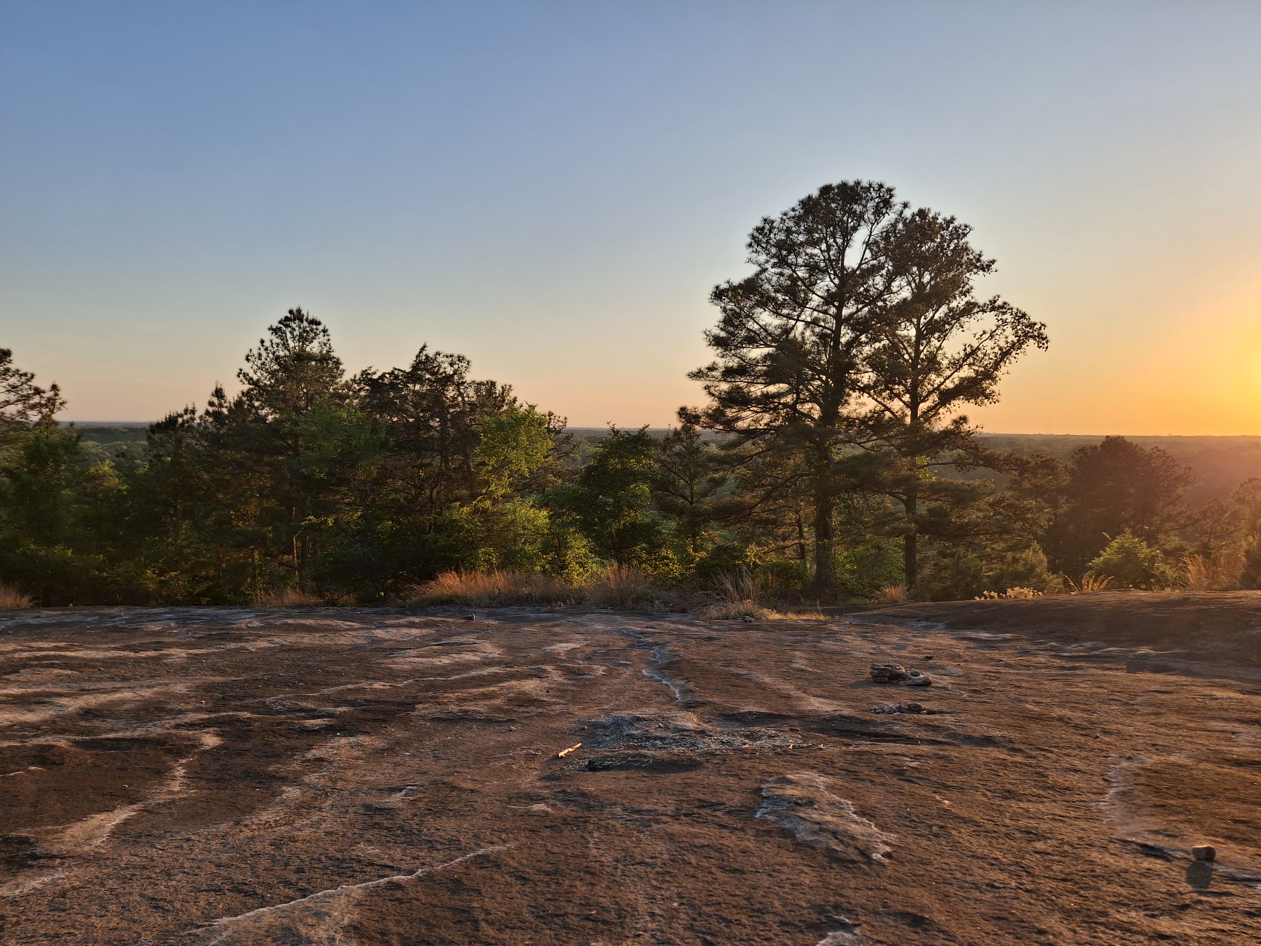 Fire-orange sunset behind silhouetted pines, cracked granite in the foreground.