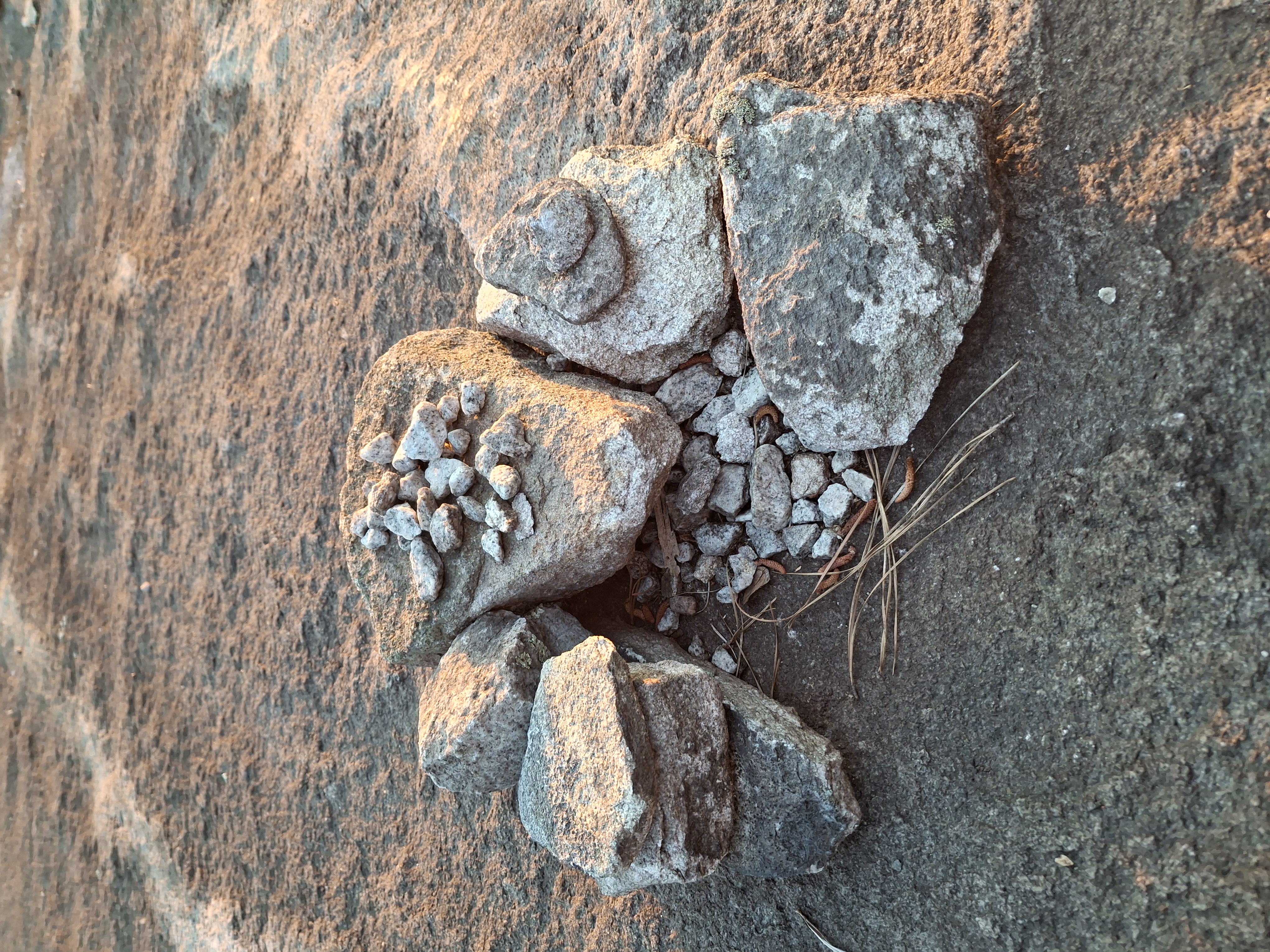 A small cairn of placed granite shards with a handful of light-gray pebbles heaped on one stone.