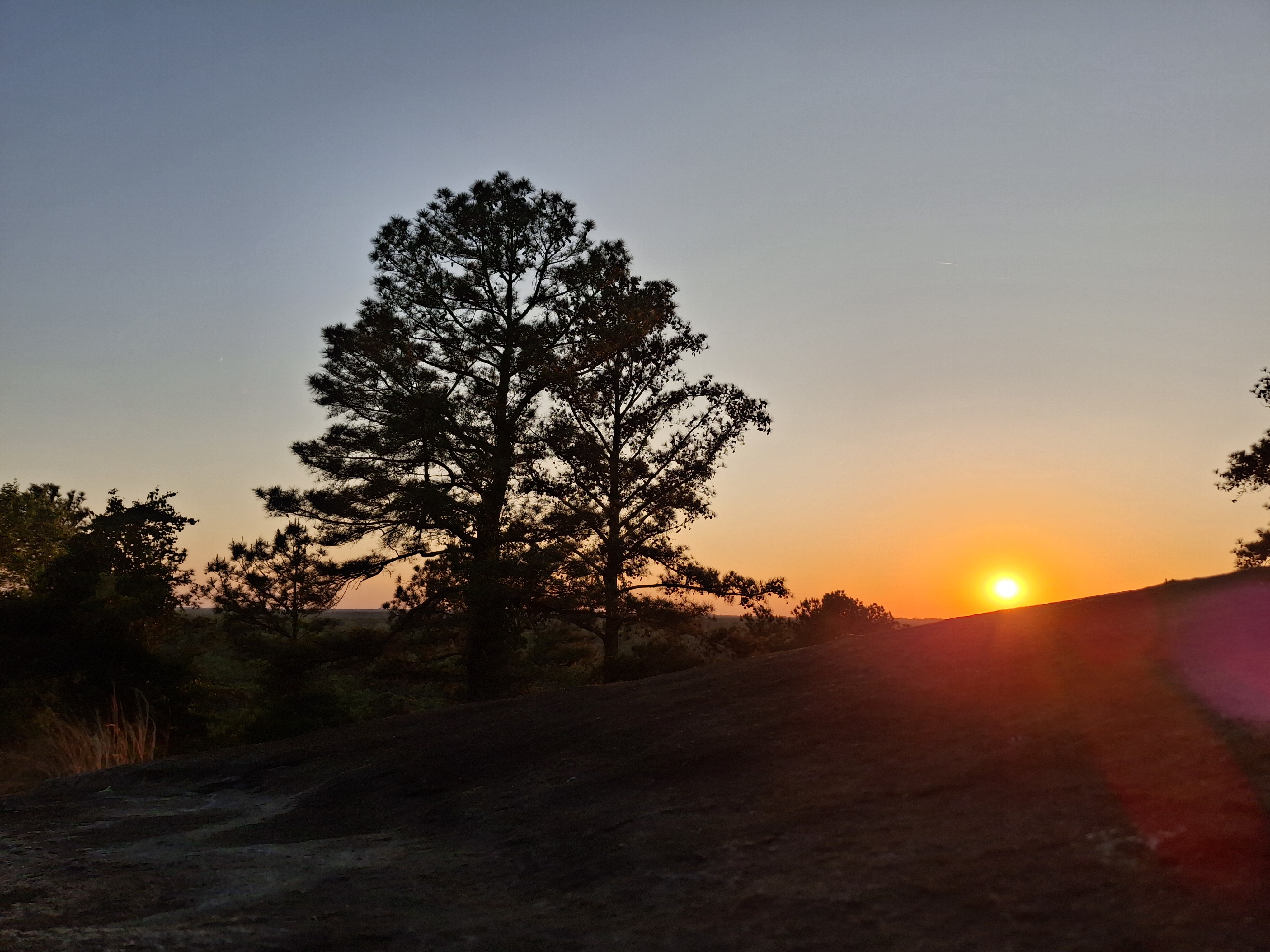 The sun low at the horizon, pines silhouetted, granite slope falling into the frame.