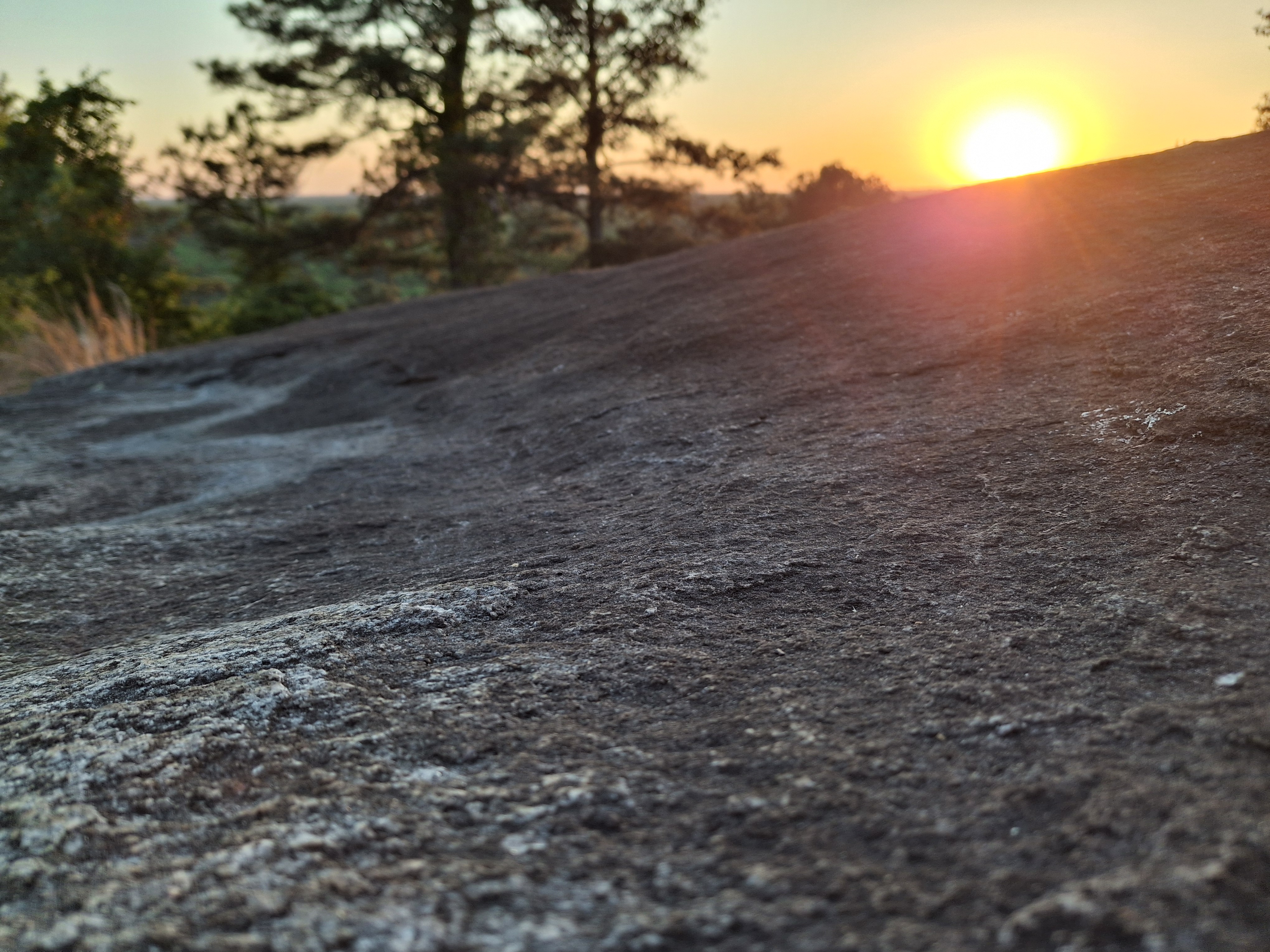 Extreme close-up of the granite grain, a ridge of stone running across the frame with sun flare at the top edge.